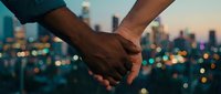 Interracial couple holding hands against a glowing city skyline at dusk, symbolizing love, unity, and togetherness in an urban setting.