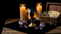 Mystical fortune telling setup with crystal ball, tarot cards, amethyst crystals and candles on wooden table for divination and spiritual guidance sessions.