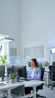 Young professional woman with headset working at computer in modern office with holographic data displays and analytics charts.