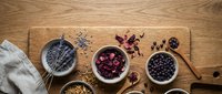 Assorted superfoods in wooden bowls on rustic table including chia seeds, goji berries, blueberries and grains for healthy cooking and nutrition.