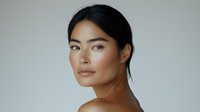 Young Asian woman with natural makeup and glowing skin against neutral gray background, side profile portrait showcasing minimal beauty aesthetic and clean skincare.
