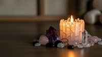 Glowing selenite candle holder surrounded by healing crystals including amethyst and rose quartz creating peaceful meditation atmosphere for spiritual wellness practices.