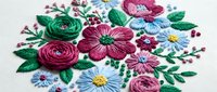 Colorful floral embroidery with roses and daisies on white fabric. Hand-stitched needlework featuring pink, green, and blue threads in traditional style.