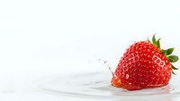 Fresh ripe strawberry splashing into clear water creating ripples and droplets on clean white background for healthy eating concepts.
