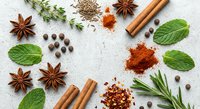 Aromatic cooking spices and herbs scattered on white surface including cinnamon sticks, star anise, paprika powder, fresh mint leaves and rosemary for culinary use.
