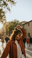 Young woman with curly hair touching her head while walking through historic European town square during golden hour sunset with warm autumn light.