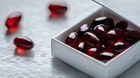 Red gel capsules in white box with scattered pills on marble surface, suitable for pharmaceutical, wellness, supplement and healthcare marketing materials.