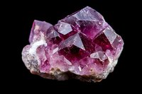 Pink and purple amethyst crystal cluster formation with geometric facets and translucent surfaces against dark background, showing natural mineral growth patterns.