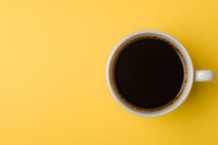 White ceramic cup filled with black coffee on vibrant yellow background, top view with copy space. Minimalist composition for cafe and restaurant marketing.