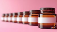 Row of amber glass medicine jars with blank white labels arranged in diminishing perspective on pink background, creating minimalist pharmaceutical composition.