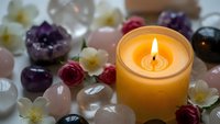 Burning candle surrounded by healing crystals, gemstones and flowers creating peaceful meditation and wellness atmosphere for spiritual practices.