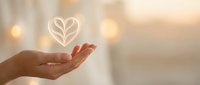 Hand holding glowing heart with leaf symbol representing eco-friendly love, sustainability and environmental care concept on warm bokeh background.