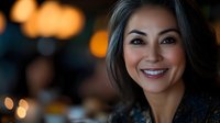 Smiling young Hispanic woman with long brown hair in elegant restaurant setting with warm bokeh lights creating cozy dining atmosphere for hospitality marketing.