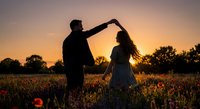 Romantic couple dancing in wildflower field at golden hour sunset, silhouetted against warm sky. Love, romance and connection in nature during spring bloom.
