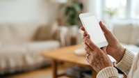 Senior woman with wrinkled hands holding blank tablet device in modern living room interior. Elderly female using digital technology at home for communication, entertainment, or online shopping.