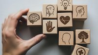 Hand selecting wooden blocks with mental health and wellness icons including brain, lightbulb, heart, and tree symbols for therapy concepts.