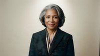Professional African American senior businesswoman in dark suit with confident expression against neutral background for corporate presentations.