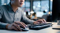 Young Asian businessman working on computer with digital interface icons displaying time management and search functions in modern office environment.