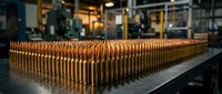 Rows of golden glass bottles on industrial conveyor belt in modern manufacturing facility for beverage production and packaging operations.