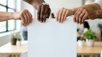 Diverse group of people holding blank white poster together in office, teamwork and collaboration concept for business presentations and corporate messaging.