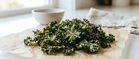 Crispy baked kale chips seasoned with herbs on parchment paper in bright kitchen setting for healthy snacking and clean eating lifestyle content.