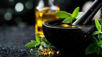 Black stone mortar with fresh herbs and olive oil on dark textured background with bokeh lights, aromatic spices and ingredients for cooking or spa treatment.