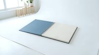 Open spiral notebook with blue and beige pages on white desk in bright minimalist workspace with plant and wooden accessories for office planning.