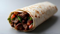 Grilled beef burrito wrapped in flour tortilla with fresh vegetables, tomatoes and herbs on gray background, appetizing Mexican fast food closeup.