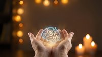 Cupped hands holding glowing brain with gears and cogs floating above palms against warm bokeh lights background for creativity and innovation concepts.