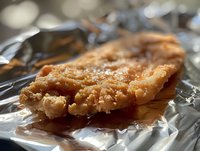 Crispy breaded chicken cutlet with golden-brown crust served on aluminum foil, close-up view showing juicy texture and crispy coating in natural lighting.
