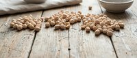 Dried chickpeas scattered on rustic wooden surface with neutral fabric and ceramic bowl, suitable for food photography, cooking blogs, and nutritional content.