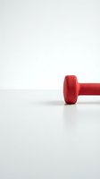 Red dumbbell weight on white surface against neutral background, isolated for fitness, gym, and workout design projects.