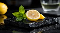 Fresh lemon half with mint leaves on dark slate board for culinary presentations and healthy lifestyle concepts.