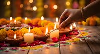 Hand lighting candles surrounded by vibrant marigold flowers and colorful rangoli patterns during traditional Diwali celebration with warm bokeh lights.