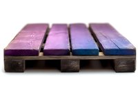 Rustic wooden pallet painted in gradient colors from purple to blue, photographed with shallow depth of field showing artistic detail and texture of wood planks.
