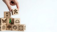 Hand placing wooden cube with puzzle piece symbol on stack of blocks featuring mental health awareness icons for wellness campaigns and therapy concepts.