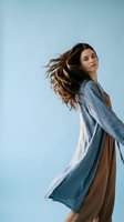 Young woman with flowing brown hair dancing in blue cardigan against clear sky background expressing joy and freedom in natural outdoor setting.