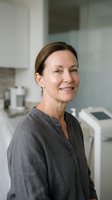 Professional middle-aged Caucasian female healthcare worker smiling confidently in modern medical office with equipment background for wellness campaigns.