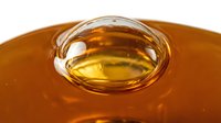 Golden honey with air bubble trapped in glass dome on white background, isolated for packaging and culinary design use.
