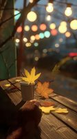 Autumn maple leaves on wooden table with coffee cup and cozy bokeh lights in background, creating warm seasonal atmosphere.