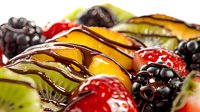 Fresh mixed fruits with dark chocolate drizzle including strawberries, kiwi, blackberries and mango slices arranged in appetizing rows, macro food photography.