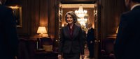 Professional middle-aged Caucasian businesswoman in dark suit standing confidently in elegant office hallway with warm lighting and wooden paneling.
