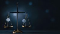 Golden scales of justice on dark blue background with bokeh lights representing legal system fairness and judicial balance in courtroom setting.
