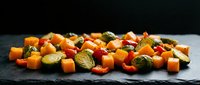 Colorful roasted autumn vegetables with butternut squash, Brussels sprouts and sweet potato cubes arranged on dark slate surface for healthy cooking.