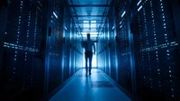 Silhouette of person walking through modern data center corridor with glowing server racks and blue lighting for technology and computing concepts.