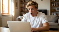 Young Caucasian man with surprised expression looking at laptop screen in modern home office. Shocked male working from home reacting to unexpected news online.