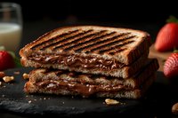 Grilled chocolate hazelnut sandwich with melted filling on dark slate, surrounded by fresh strawberries and nuts for gourmet breakfast or dessert concept.