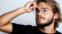 Young thoughtful Caucasian man with glasses and beard touching forehead in contemplative pose against white background for business concepts.