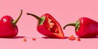 Fresh red bell peppers sliced and whole on pink background for cooking and healthy eating concepts.