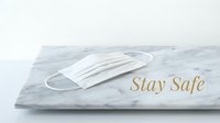 White medical face mask on marble surface with gold Stay Safe text, health protection concept on light background.